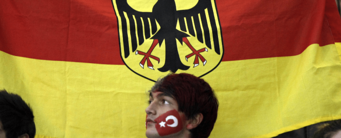 Vor der deutschen Flagge ein Mann, der eine Gesichtsbemalung hat - zaman