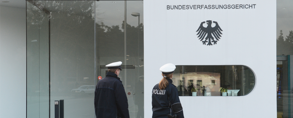 Zwei Polizisten laufen am 03.12.2013 in Karlsruhe (Baden-Württemberg) vor dem Eingang zum Bundesverfassungsgericht entlang. Nach monatelanger Vorbereitung wollen die Länder an diesem Dienstag einen neuen Verbotsantrag gegen die rechtsextreme NPD beim Bundesverfassungsgericht in Karlsruhe einreichen.