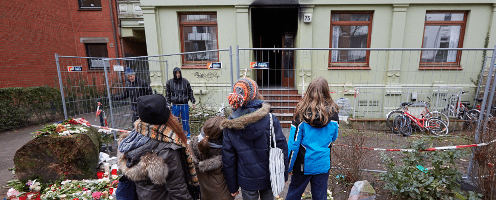 Kinder stehen am 07.02.2014 in Hamburg im Stadtteil Altona vor einem ausgebrannten Mehrfamilienhaus, das als Flüchtlingsunterkunft diente. Eine Mutter und ihre zwei Jungen sind bei einem Brand in dem Haus ums Leben gekommen.