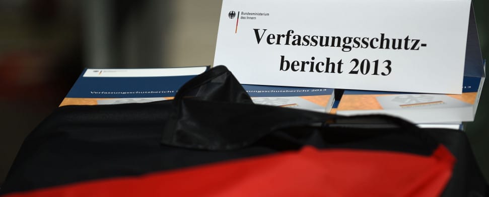 Ausgaben des Verfassungsschutzberichts 2013 liegen am 18.06.2014 zu Beginn einer Pressekonferenz in Berlin unter einer Deutschlandflagge. Der Bericht wurde vom Bundesinnenminister und dem Verfassungsschutzpräsidenten vorgestellt.