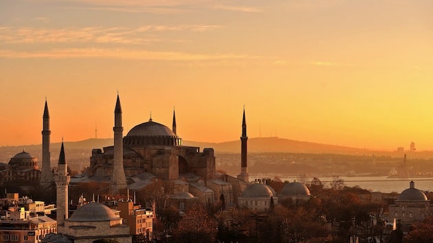 Die prächtige Hagia-Sophia prägt das Bild Istanbuls. Das Bild zeigt die Metropole am Bosporus bei Sonnenaufgang, die Hagia-Sophia erstrahlt in gelb-orange.