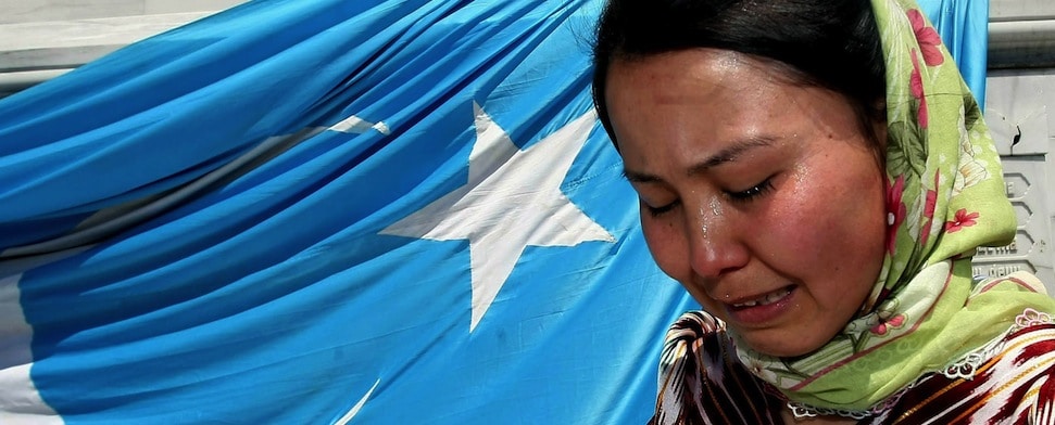 Eine uigurische Frau weint vor der blauen Flagge ihres Volkes.