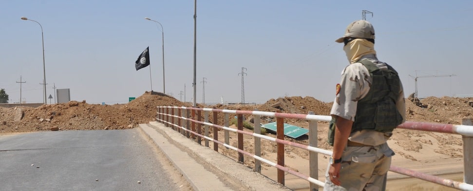 Ein kurdischer Kämpfer steht etwa 20 Meter von einer IS-Straßensperre nahe Kirkuk. Die schwarze IS-Fahne ist deutlich zu erkennen.
