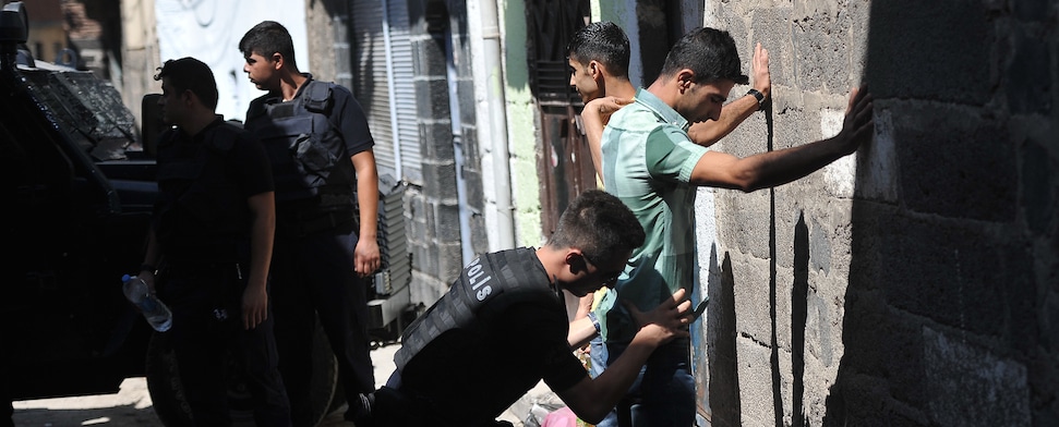 Ein türkischer Polizist durchsucht einen jungen Mann in einer Gasse.
