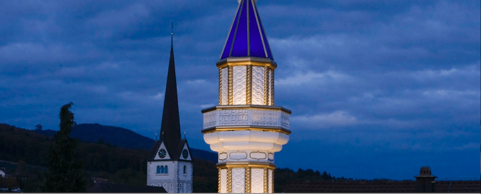 Ein Minarett ist vor einem Kirchturm zu sehen.