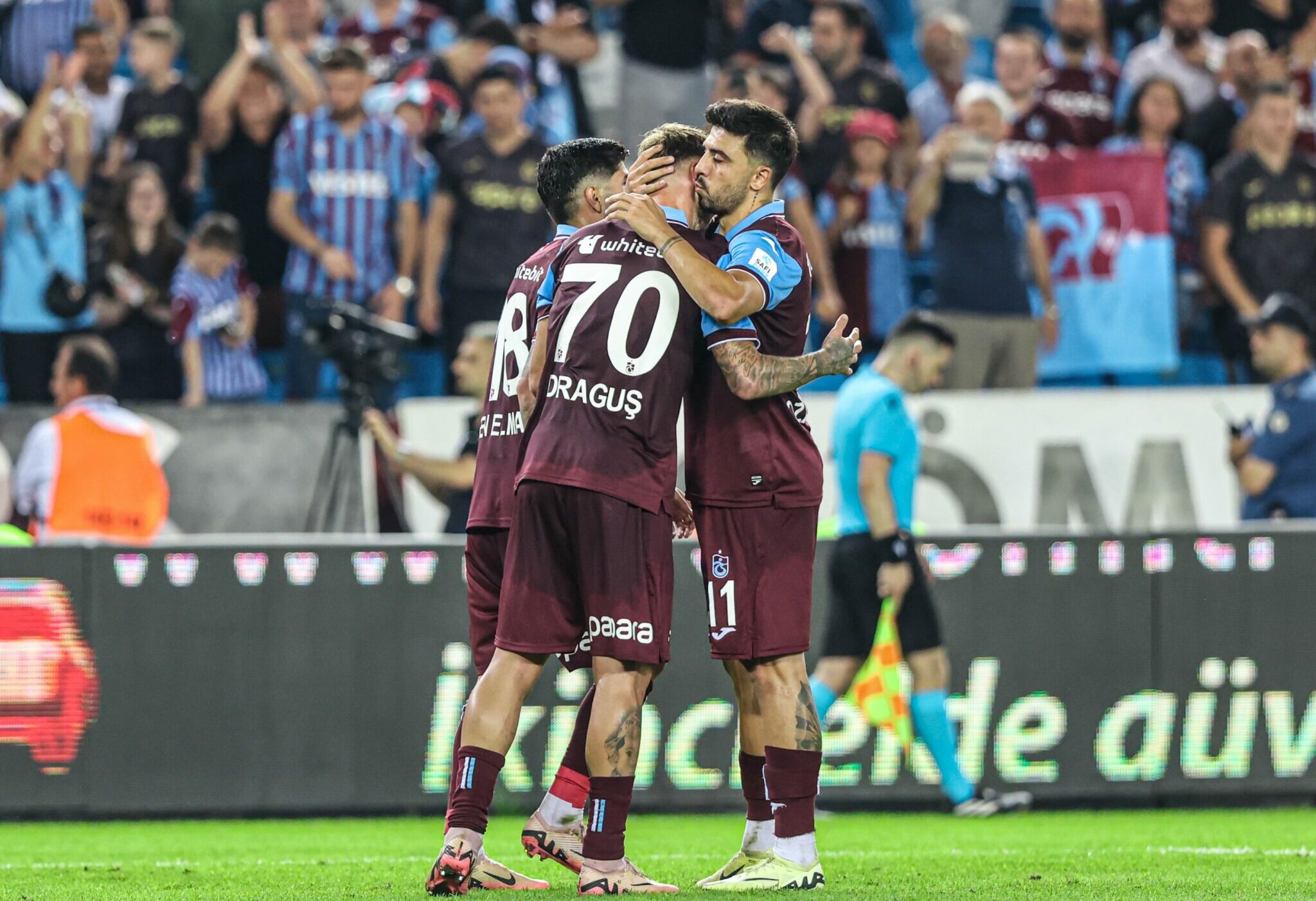 Trabzon: Ozan Tufan gratuliert Denis Draguş nach dessen Tor. Beide Spieler umarmen sich freudig, während die Fans im Hintergrund jubeln.